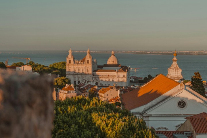 Scenic view of a coastal city with historic buildings and ocean in the background at sunset.