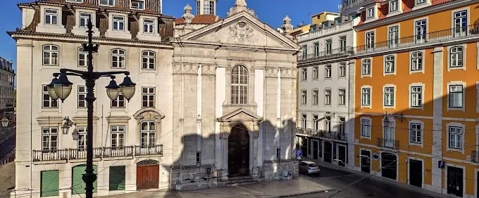 Historic church and adjacent colorful buildings under a clear blue sky on a sunny day.