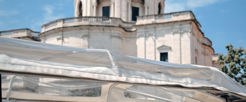 Person in striped shirt sitting in open vehicle with large domed building behind.
