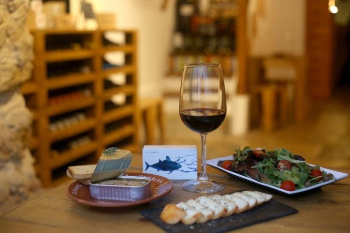 Wine glass with red wine, salad, cheese, and canned fish on a table in a cozy wine room.