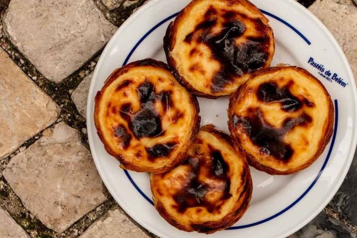 Four pastel de nata on a plate with cobblestone background.