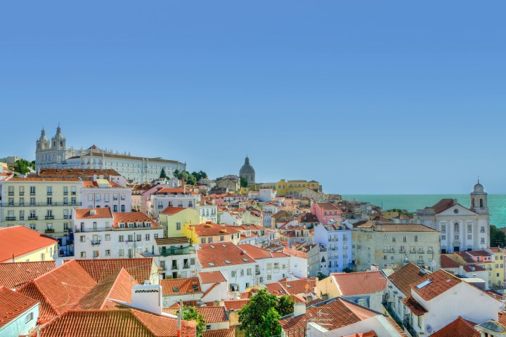 Colorful rooftops and historic buildings overlook the sea under a clear blue sky.
