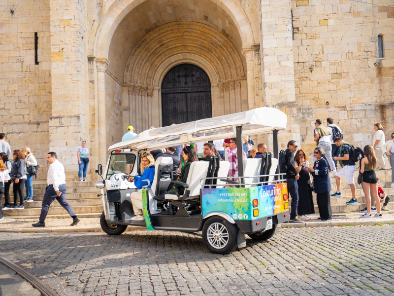 Group walking and in tuk-tuk near large stone building entrance.