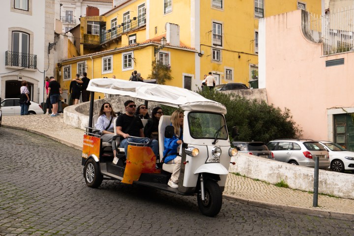 Tourists riding a tuk-tuk on a cobblestone street, yellow buildings in background.