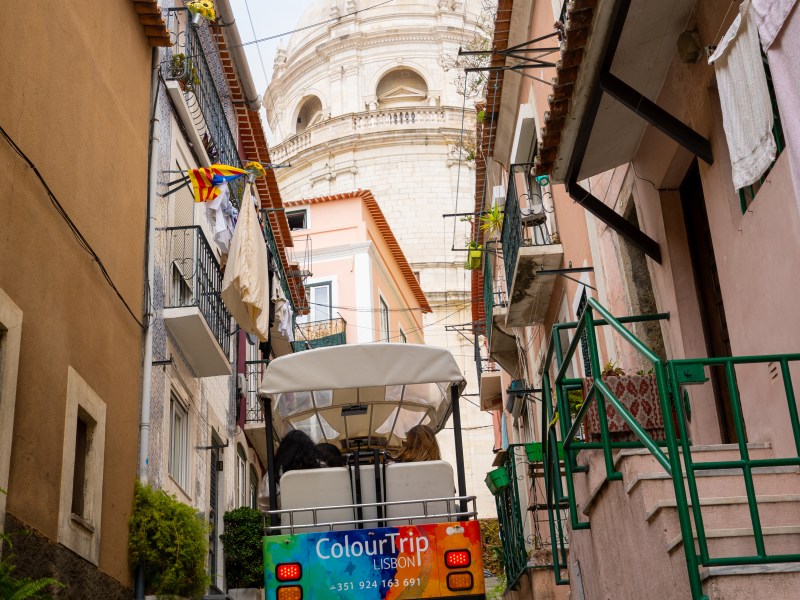 Narrow cobblestone street with a tuk-tuk and a dome in the background.