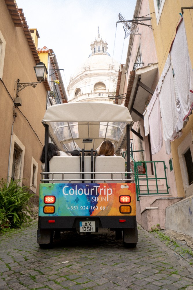 A colorful tuk-tuk on a narrow, cobblestoned street with a domed building ahead.