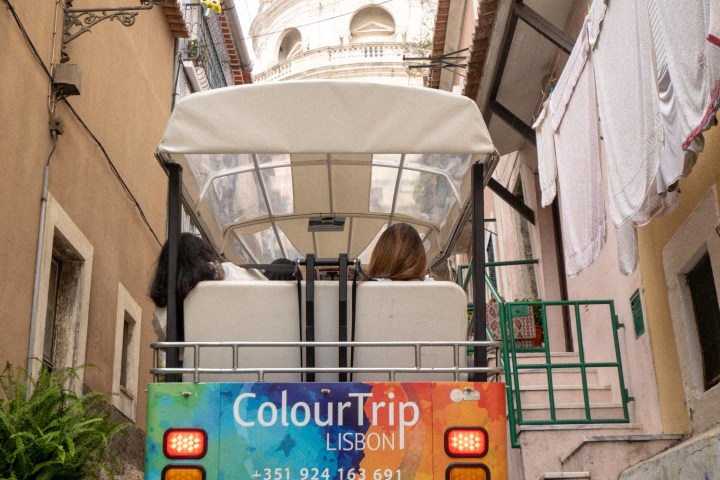 Tour cart in narrow Lisbon street with dome in background.