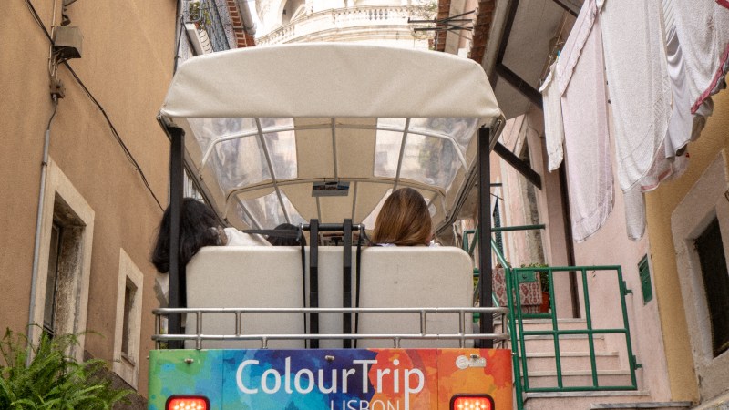 Tour cart in narrow Lisbon street with dome in background.
