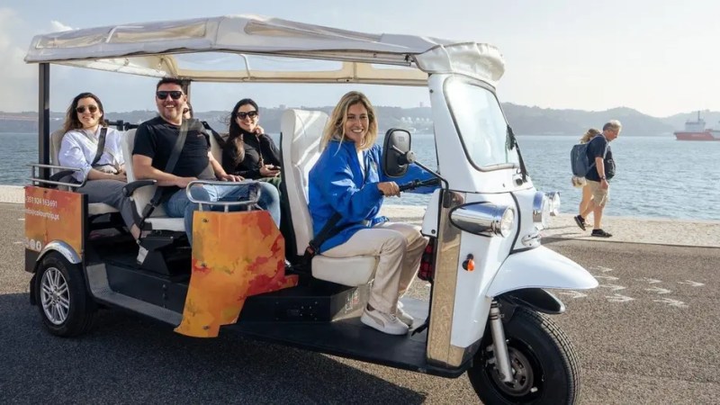 Group in a tuk-tuk by the waterfront with a smiling driver and scenic background.