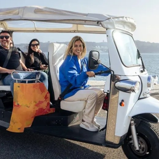 Group in a tuk-tuk by the waterfront with a smiling driver and scenic background.