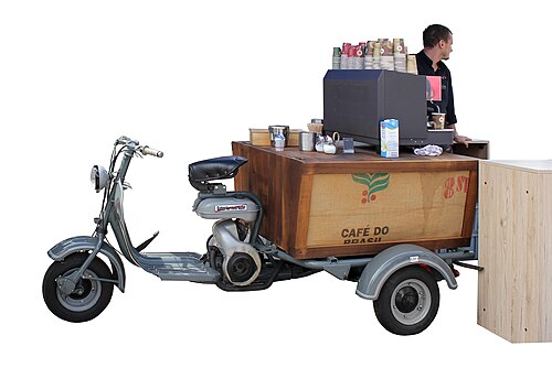 Converted scooter coffee cart with supplies and a person standing behind.