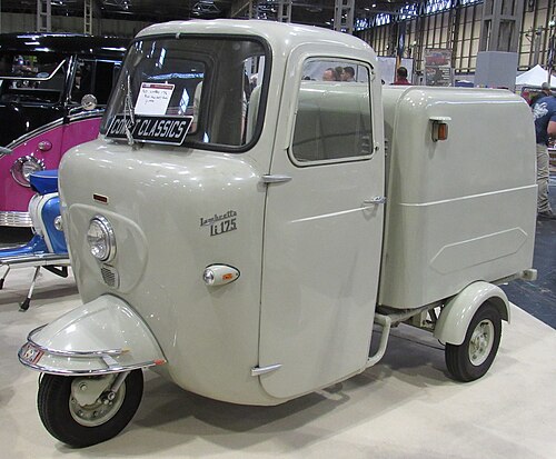 Vintage three-wheeled vehicle with a cab and cargo area on display indoors.