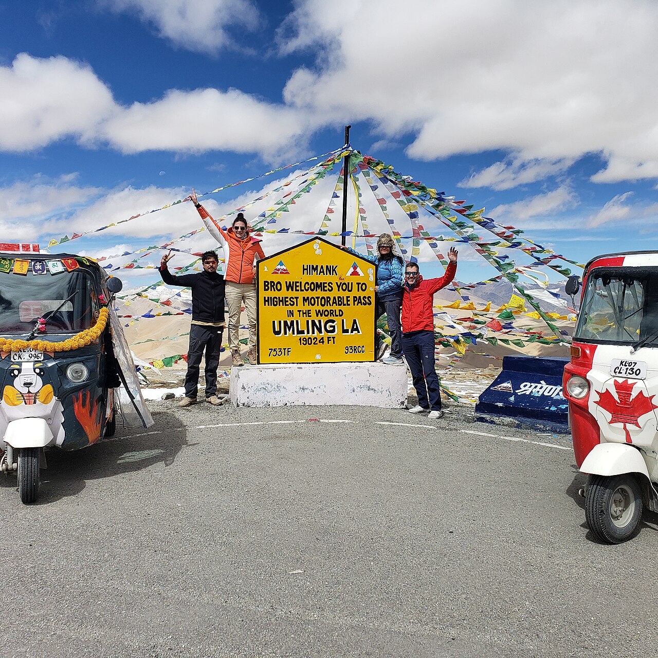 Group poses at Umling La, high motorable pass, with tuk-tuks and prayer flags.