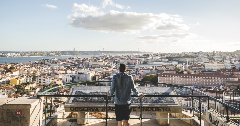 Person overlooking cityscape from a high viewpoint, with railing and informational display.