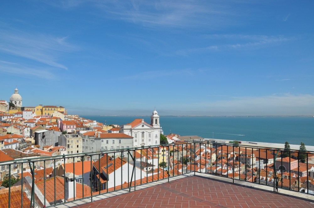 Overlook with city rooftops, ocean, and blue sky.