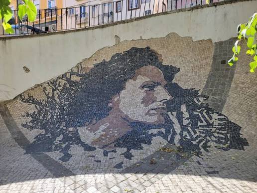 Mosaic portrait of a person on a curved outdoor wall.