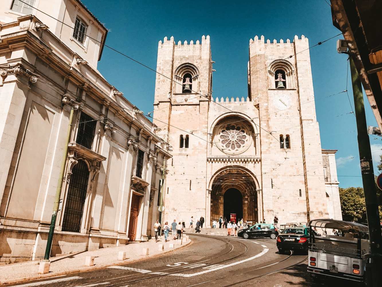 Street view of a historic stone cathedral with twin towers under a clear blue sky.