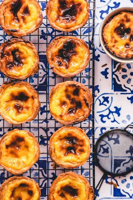 Portuguese egg tarts on a cooling rack over blue patterned tiles.